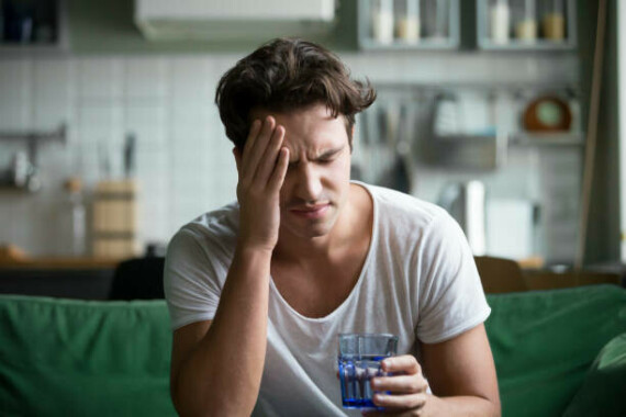 Young man suffering from headache, migraine or hangover at home Young man suffering from strong headache or migraine sitting with glass of water in the kitchen, millennial guy feeling intoxication and pain touching aching head, morning after hangover concept drink drug stock pictures, royalty-free photos & imagesNguồn: iStock
